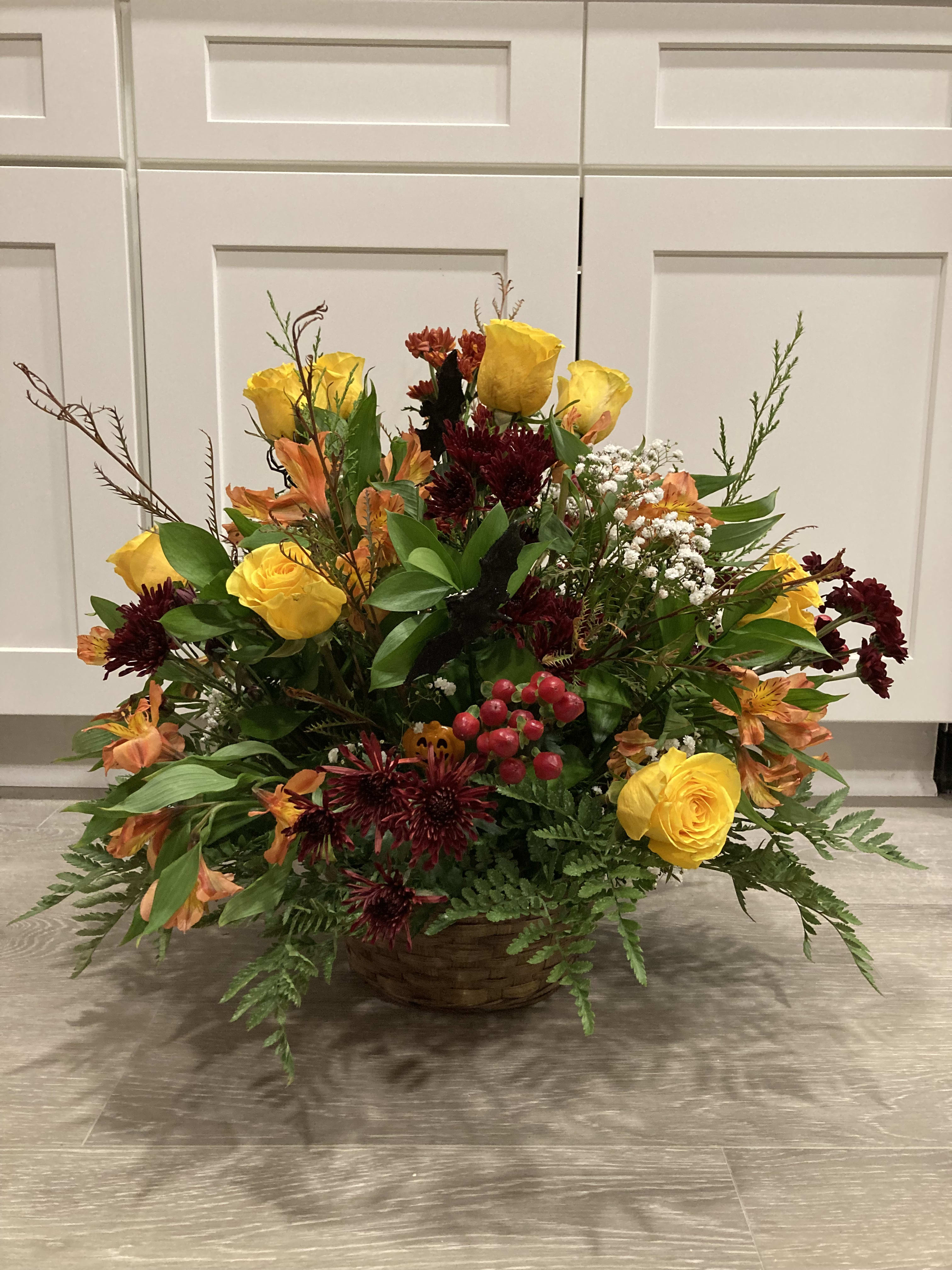 Basket arrangement of yellow roses and orange flowers with burgundy blooms
