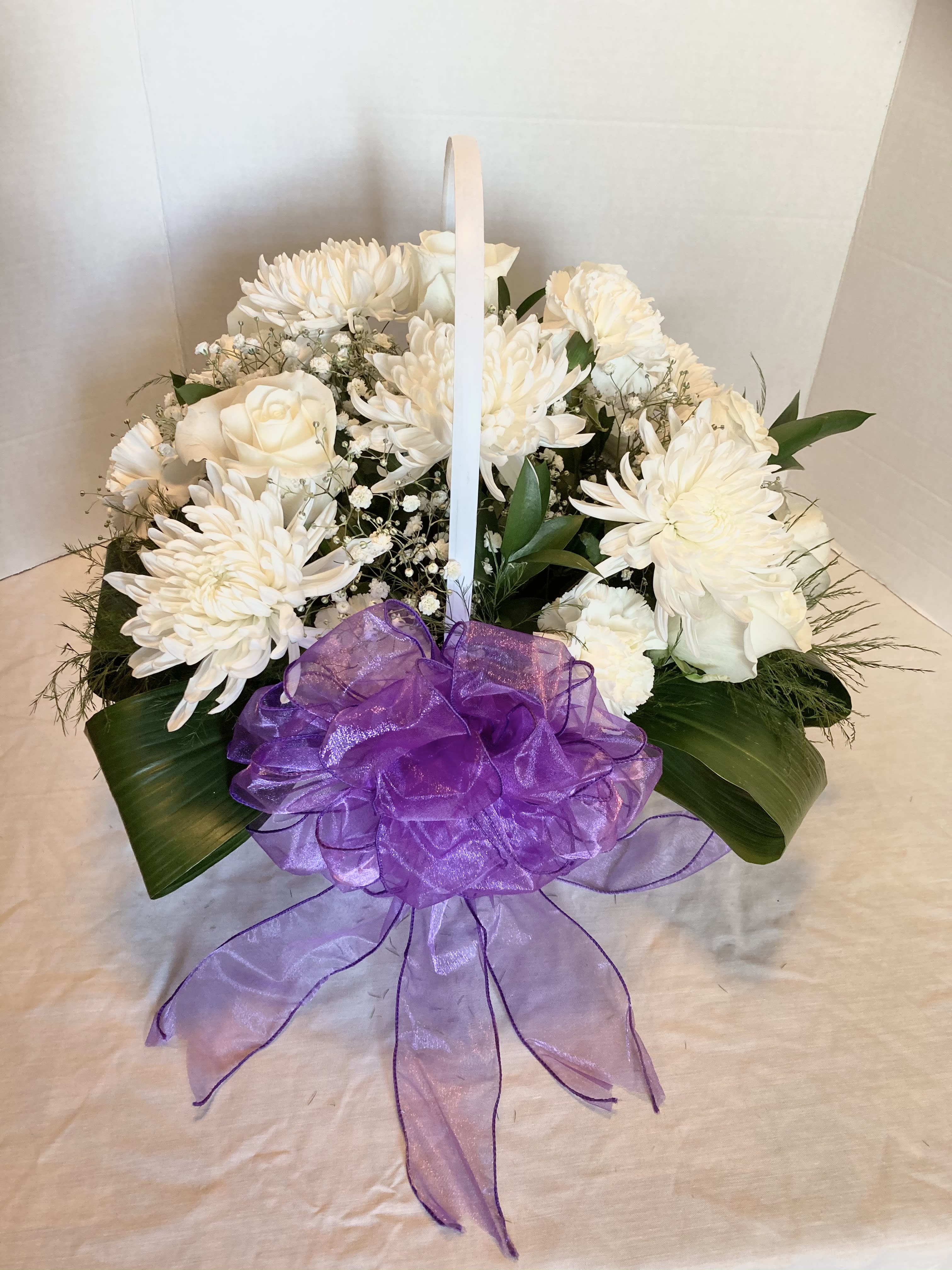 White floral basket arrangement with a purple ribbon bow
