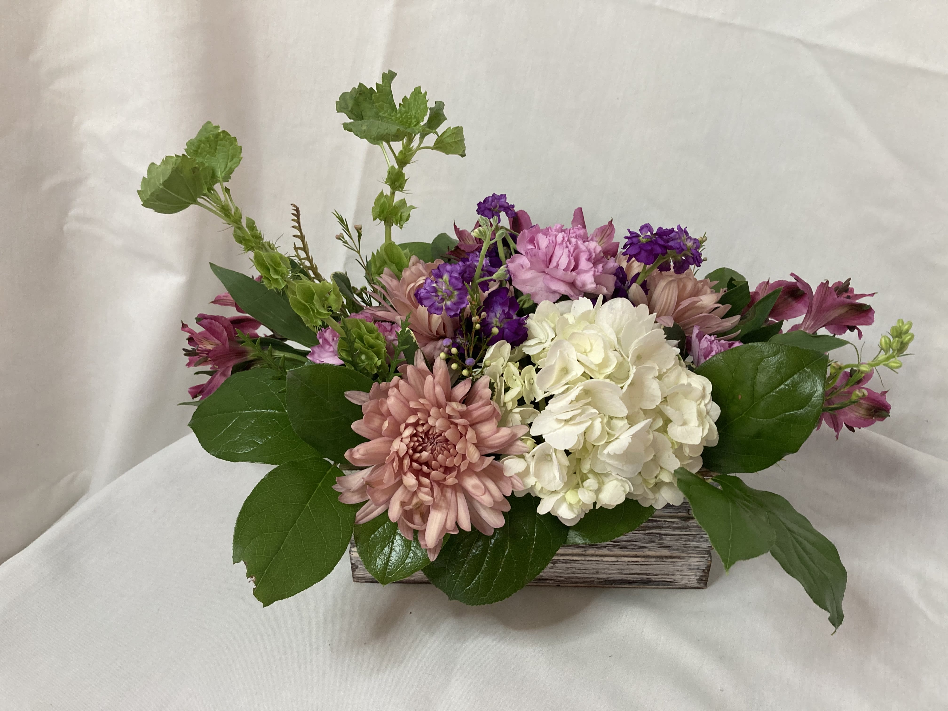 Mixed pink, white, and purple flowers arranged in a low wooden container