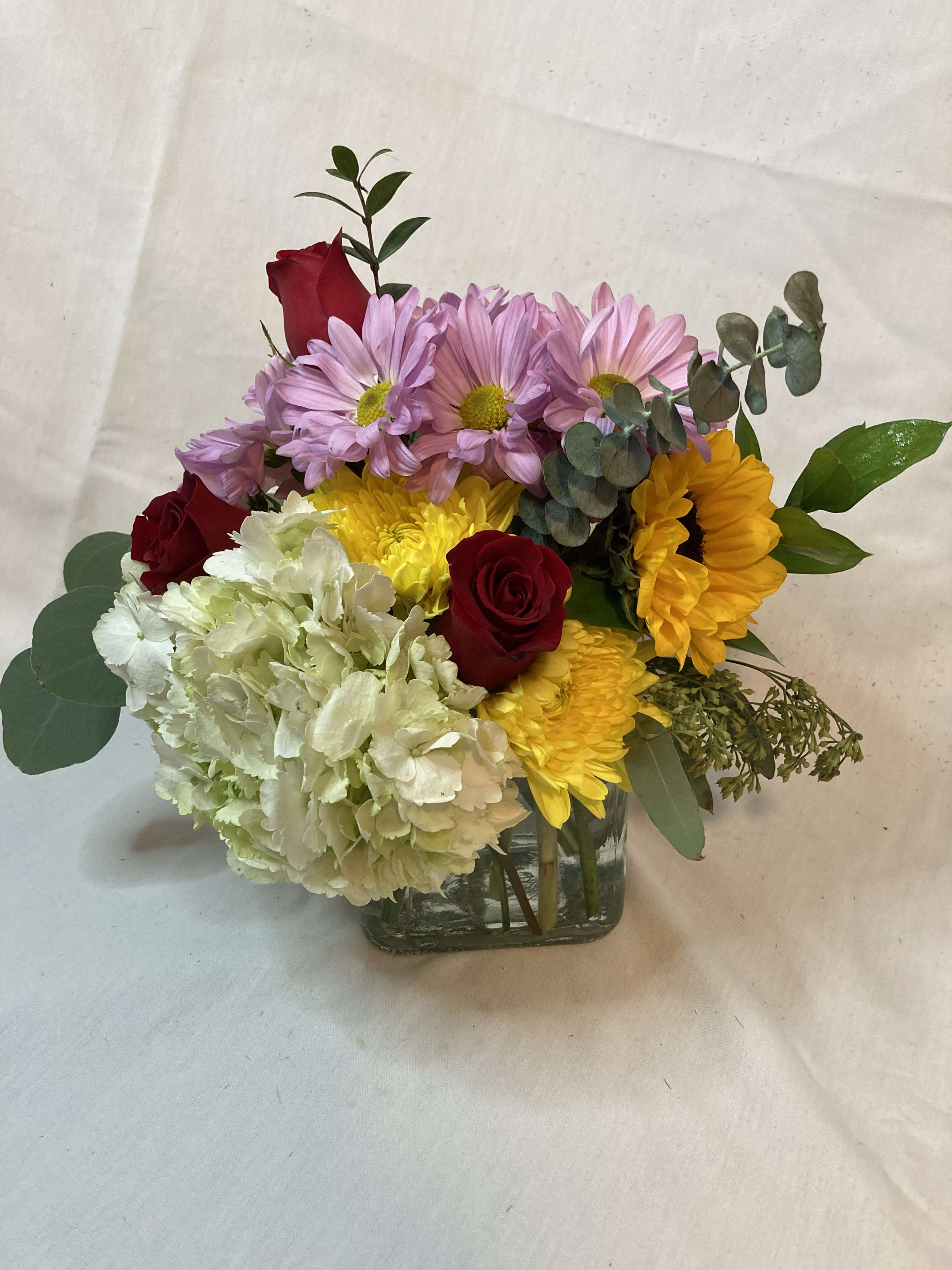 Mixed bouquet of roses, daisies, hydrangea, and sunflowers in a glass vase