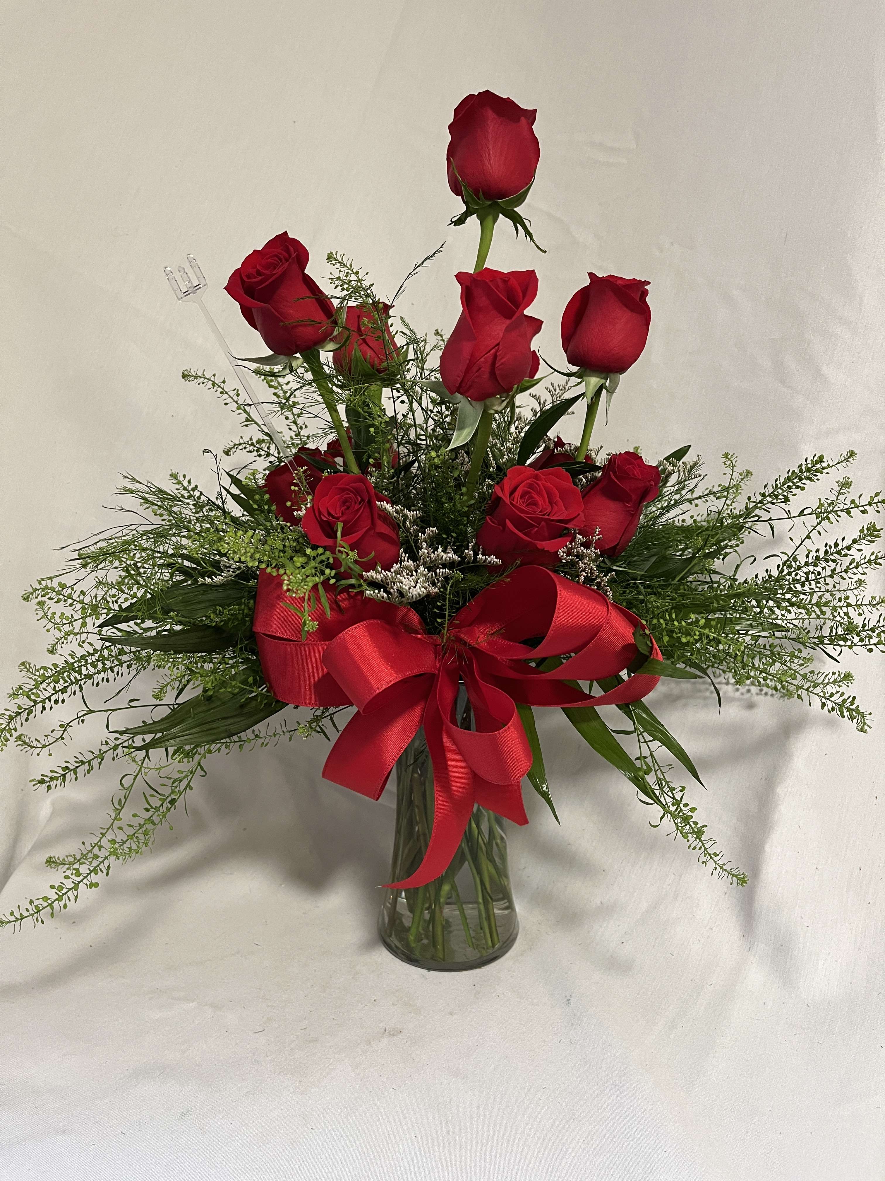 Red roses arranged in a clear glass vase with a large red ribbon