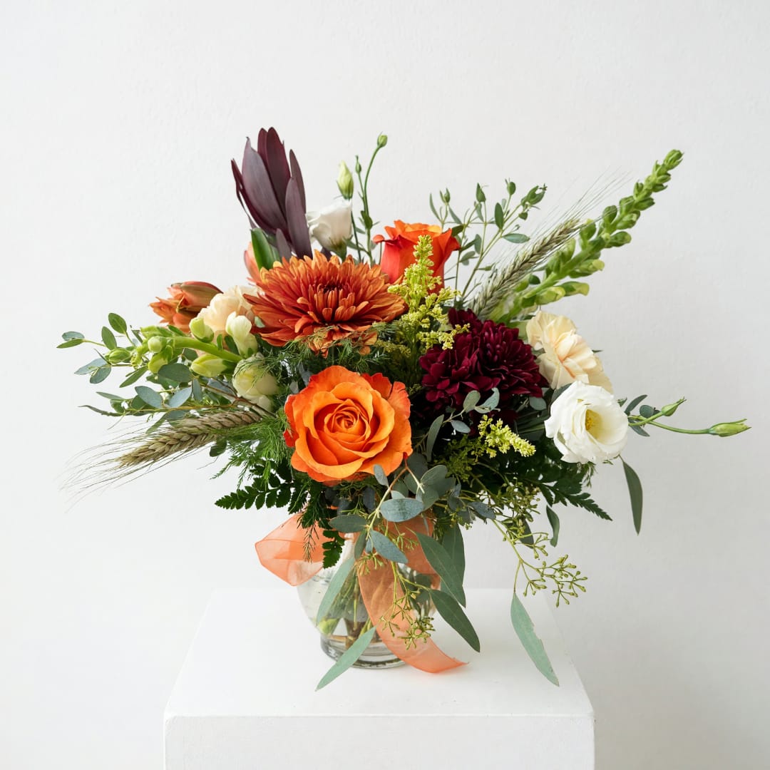 Mixed bouquet of orange, burgundy, and white flowers in a glass vase