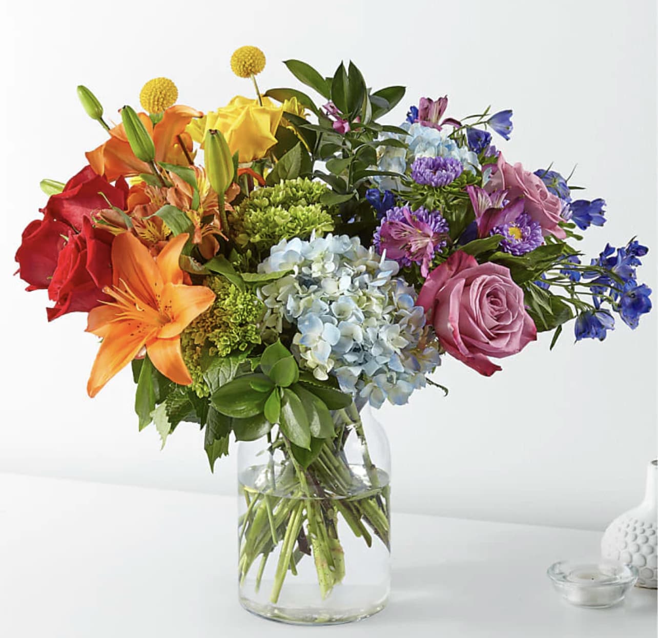 Mixed bouquet of roses, lilies, hydrangeas, and other flowers in a glass vase