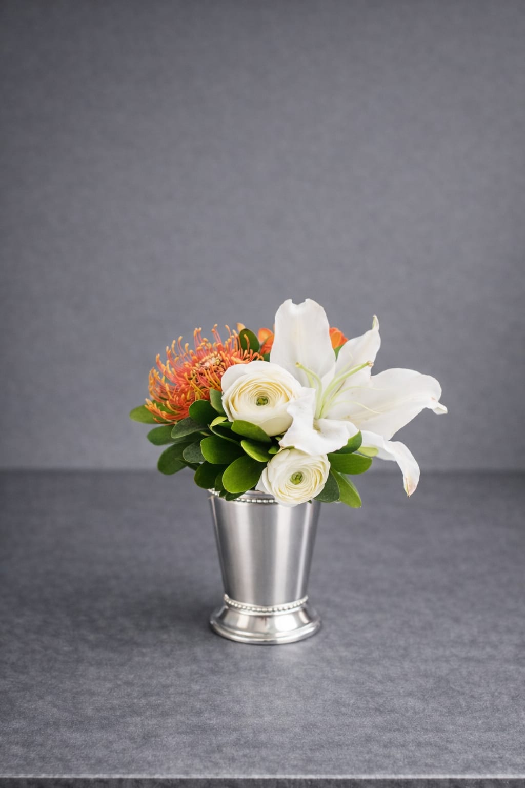 White lilies and ranunculus in a silver vase with orange blooms