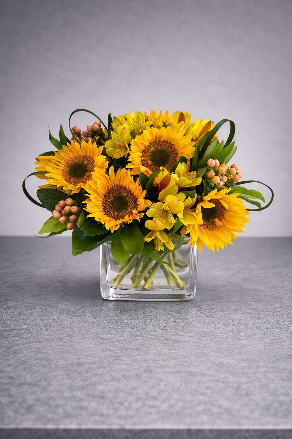 Sunflower bouquet in a clear square vase with yellow filler flowers