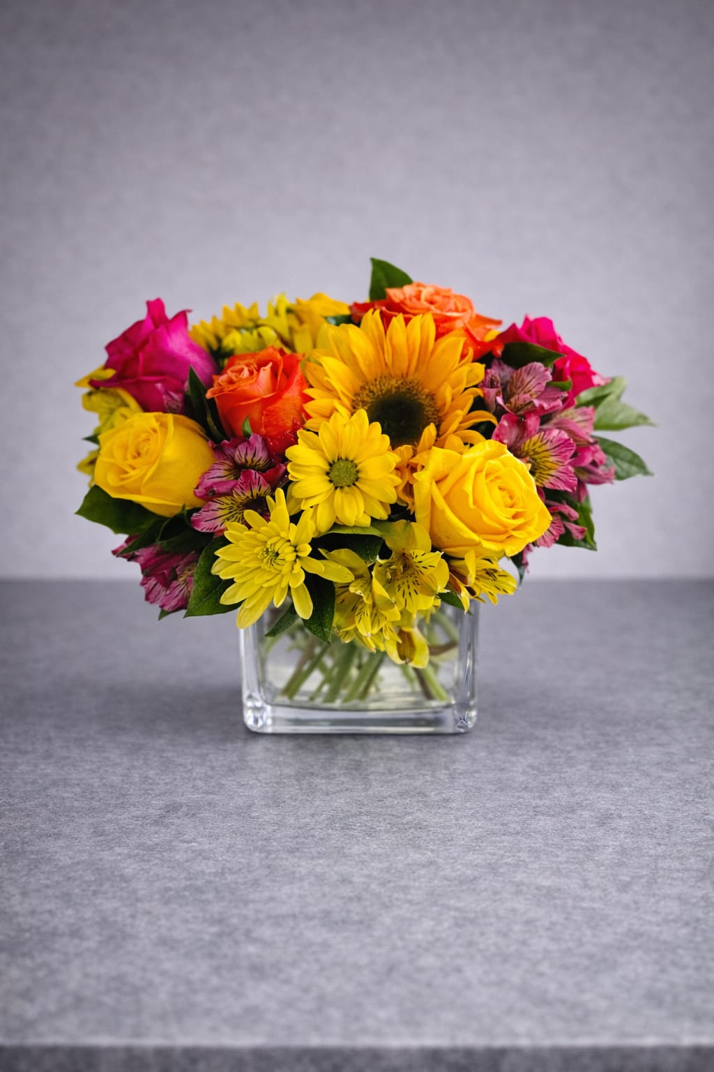 Colorful bouquet of roses, sunflowers, and daisies in a clear glass vase