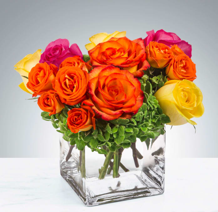 Bright Morning by BloomNation™ - Pink, yellow and orange roses and spray roses come together with green hydrangea for a bright cube of sunshine. This arrangement lights up any space and will improve anybody's day. A perfect gift for all occasions.   APPROXIMATE DIMENSIONS 10" W X 11" H 