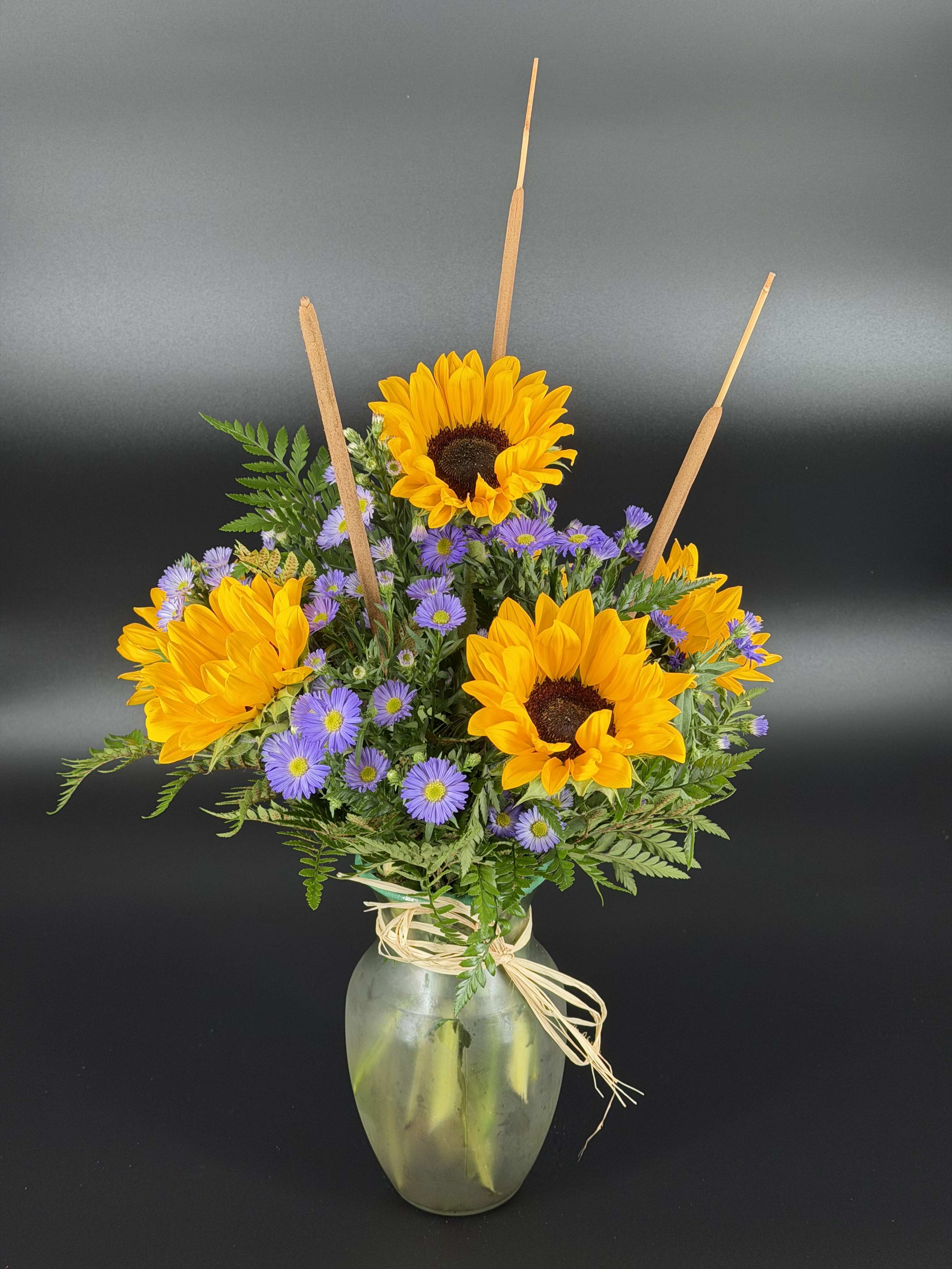 Sunflowers and purple daisies in a glass vase with raffia tie