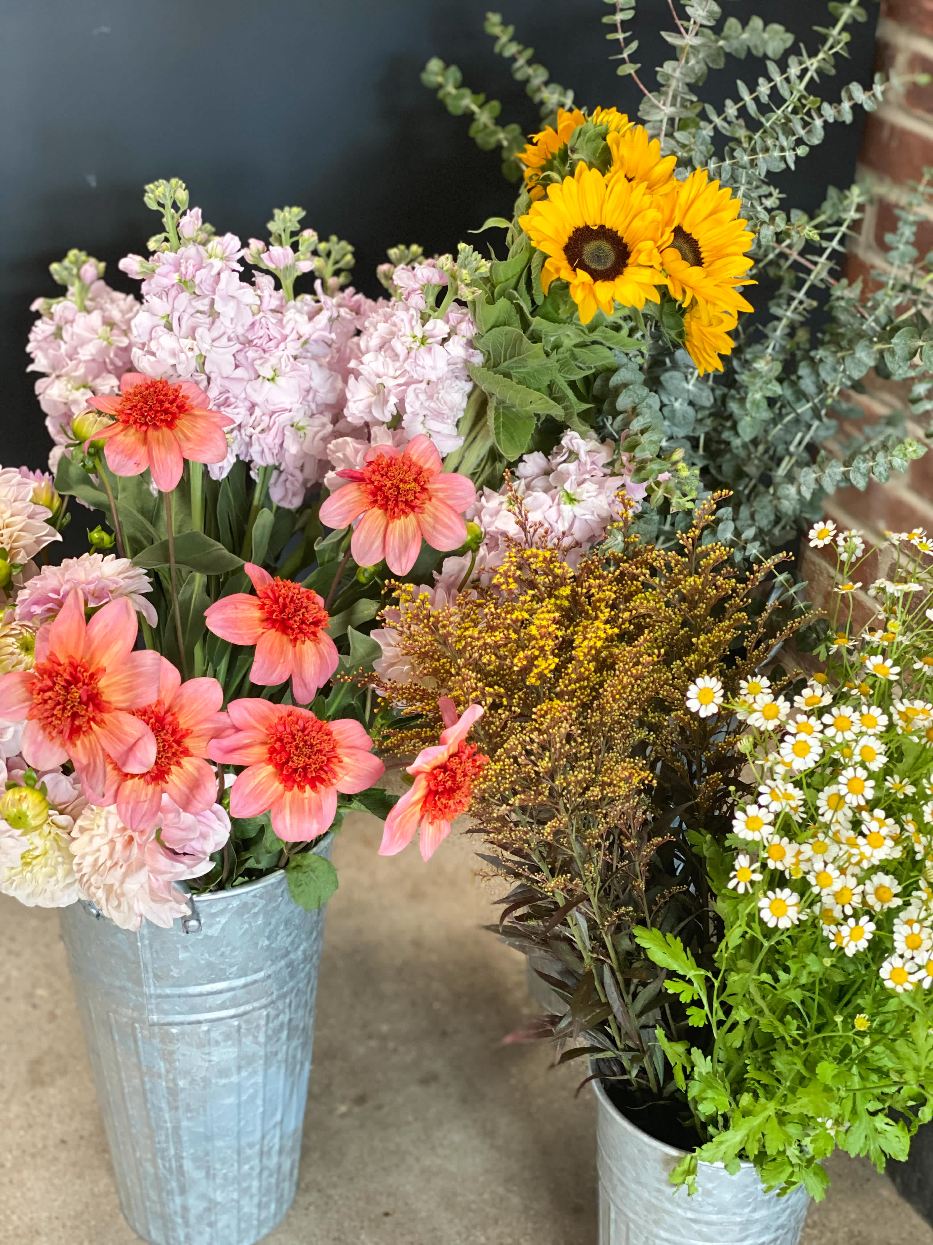 Mixed flower arrangements in metal buckets with sunflowers and pink blooms