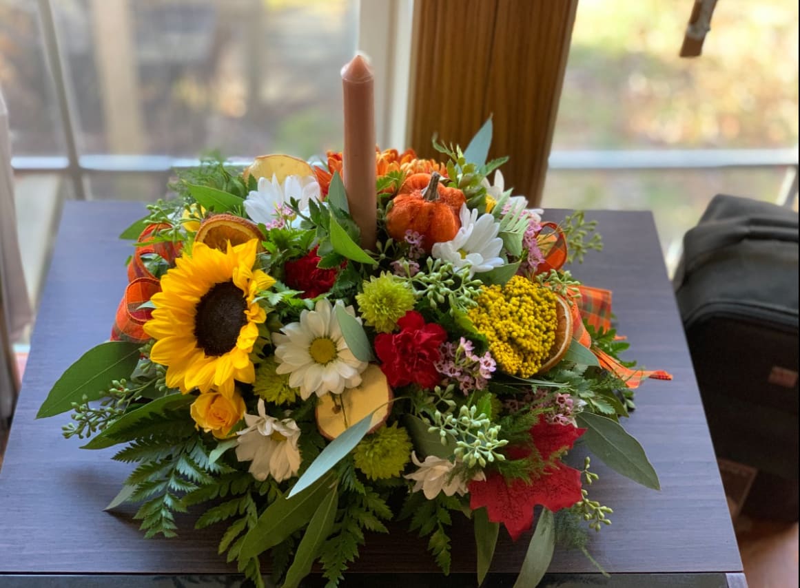 Autumn floral centerpiece with a candle, sunflowers, daisies, and small pumpkins