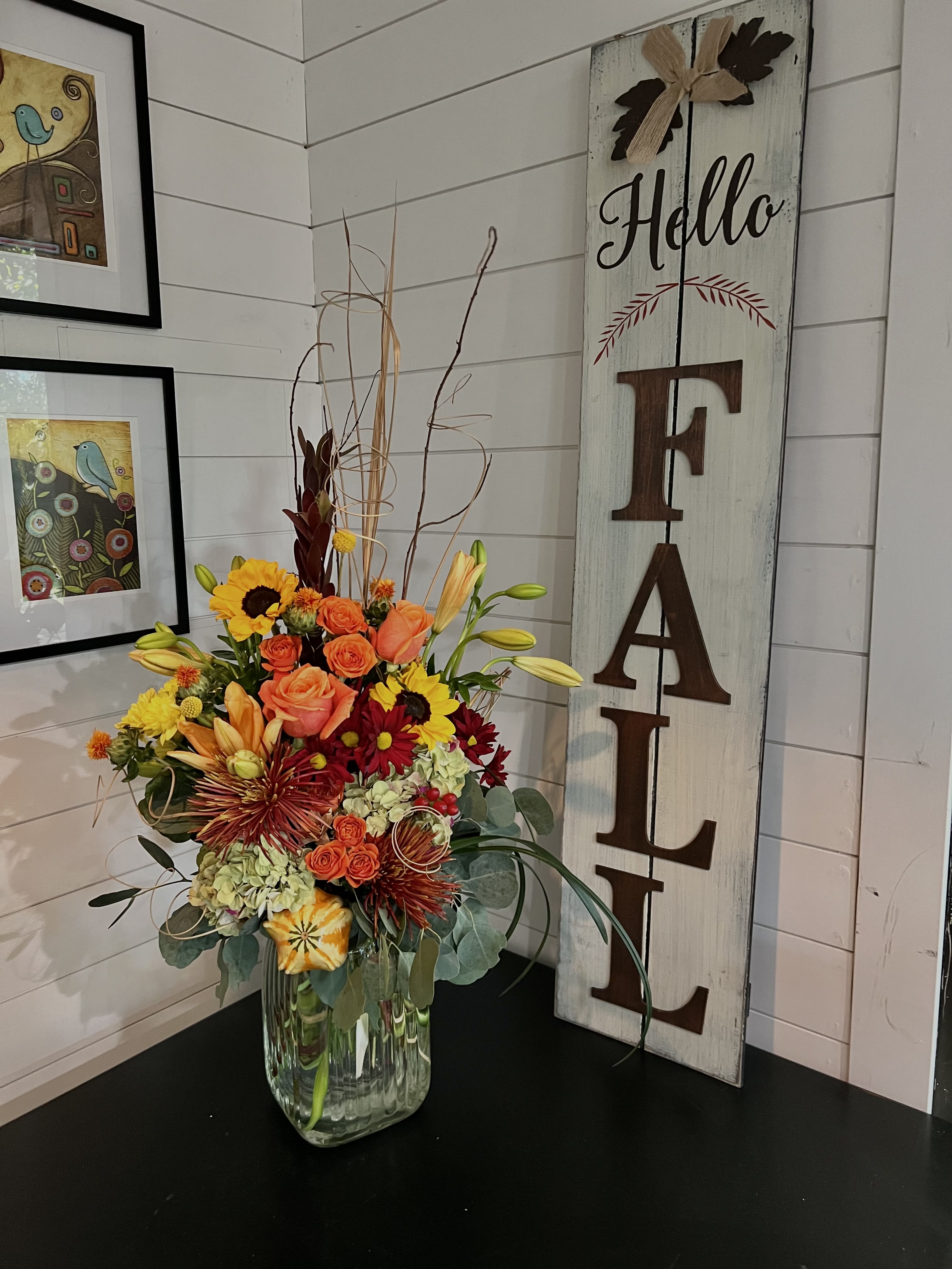 Mixed bouquet in a clear glass vase beside a vertical "FALL" sign