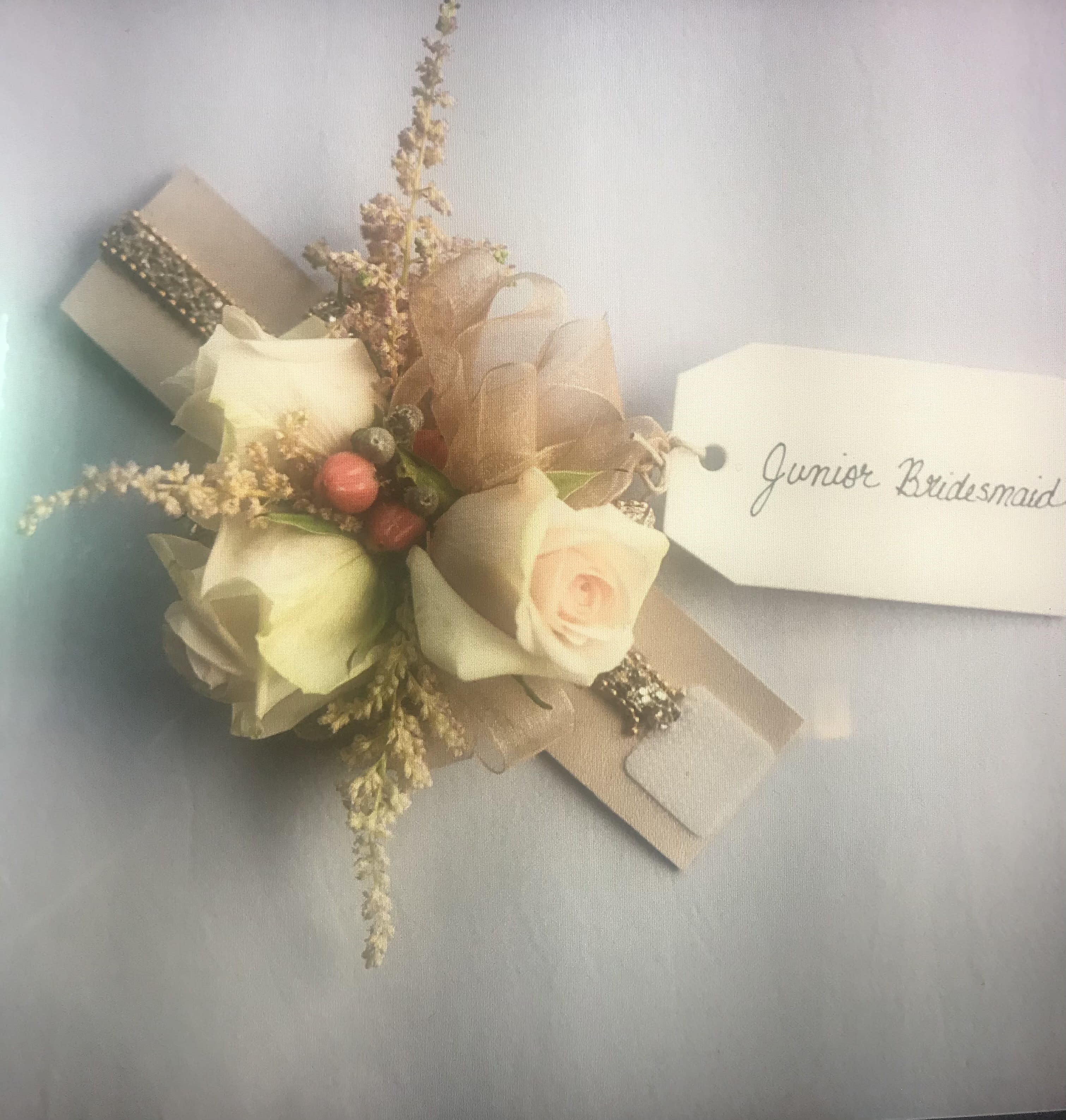 Small corsage with cream roses and a name tag reading Junior Bridesmaid