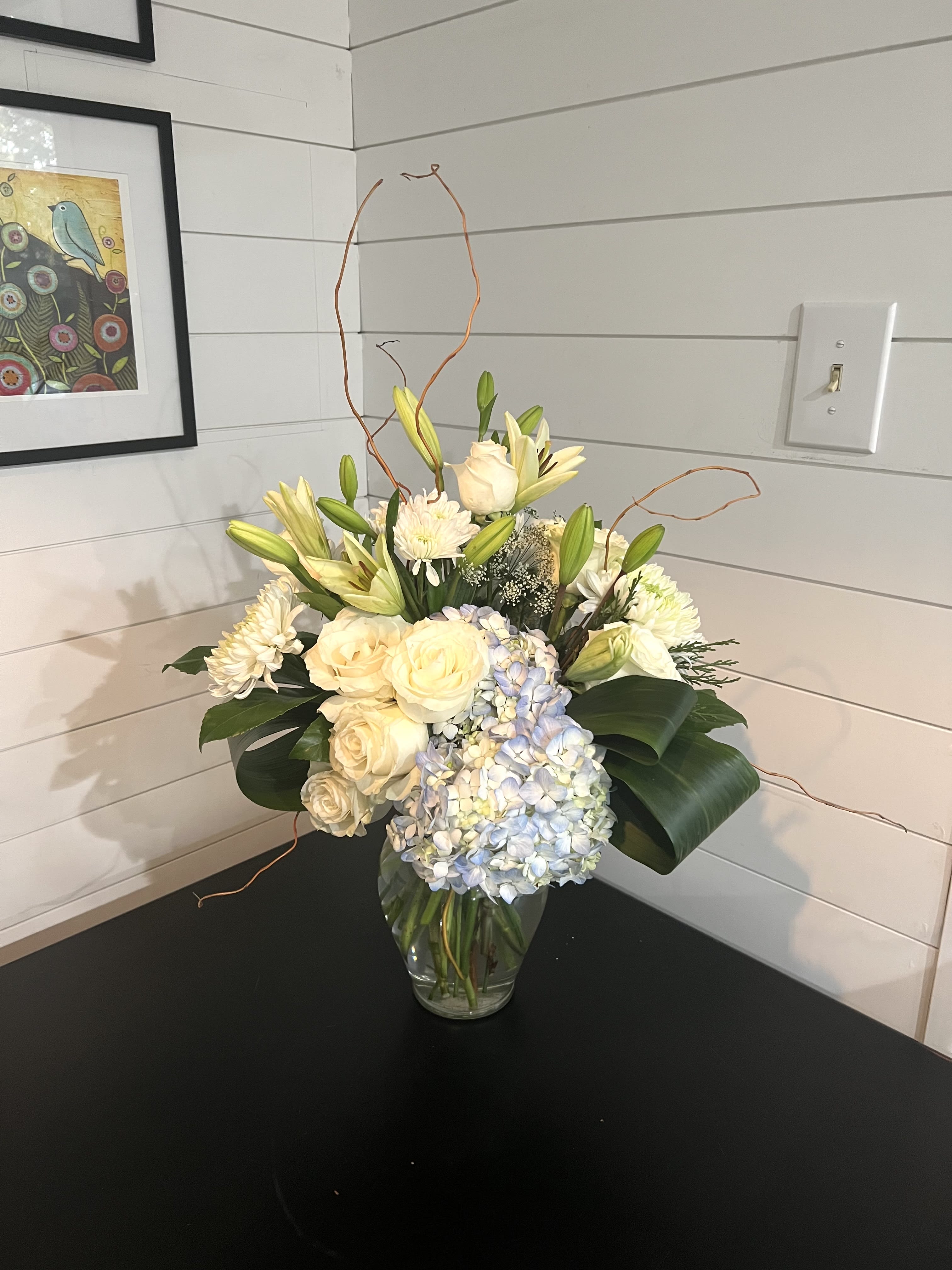 Cream roses, lilies, and blue hydrangeas in a glass vase