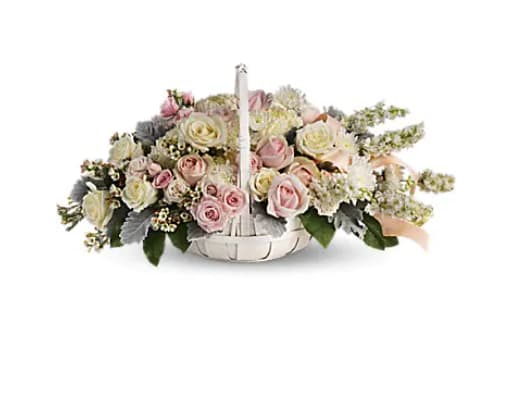 Low basket arrangement of pale pink and cream roses with white accent flowers and a peach ribbon