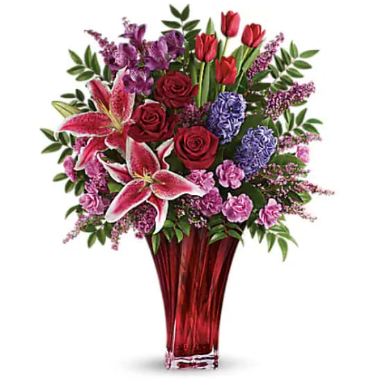 Mixed bouquet of red, pink, and purple flowers in a red glass vase