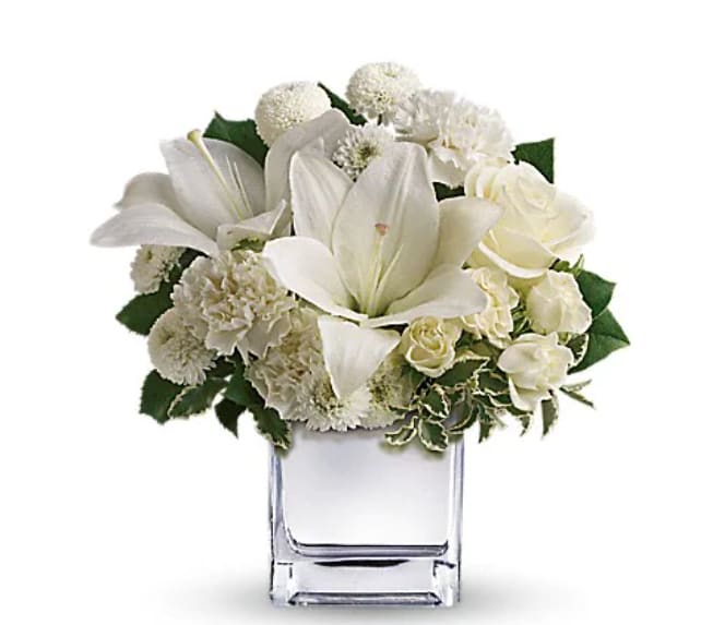 White lilies and roses arranged in a clear square vase