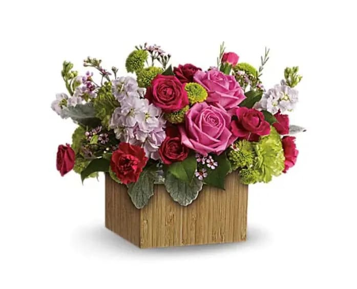 Garden Delights - Put a smile on her face and a spring in her step with this delightful little garden bouquet. Presented in a chic bamboo box, its happy hot pinks and lovely lime greens give a colorful pick-me-up! Bright pink roses and carnations are contrasted with green carnations and button spray chrysanthemums, light pink stock and delicate lavender waxflower -fresh greens include lemon leaves and soft dusty miller. Delivered in a sculptural natural bamboo vase to give it a contemporary look. 