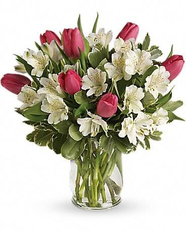 Pink tulips and white flowers arranged in a clear glass vase