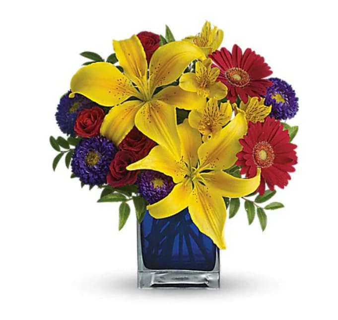 Blue Caribbean - Martinique, St. Maarten, any tropical paradise is the perfect setting for this explosively colorful bouquet in a chic blue contemporary cube vase. Can't go just now? Bring the island home. The exciting bouquet includes yellow Asiatic lilies, red miniature gerberas, purple Matsumoto asters, red spray roses and yellow alstroemeria accented with fresh greenery. Delivered in a blue contemporary glass cube vase.   Orientation : All-Around  All prices in USD ($)  Standard  T05N440A  Deluxe  T05N440B  Premium  T05N440C