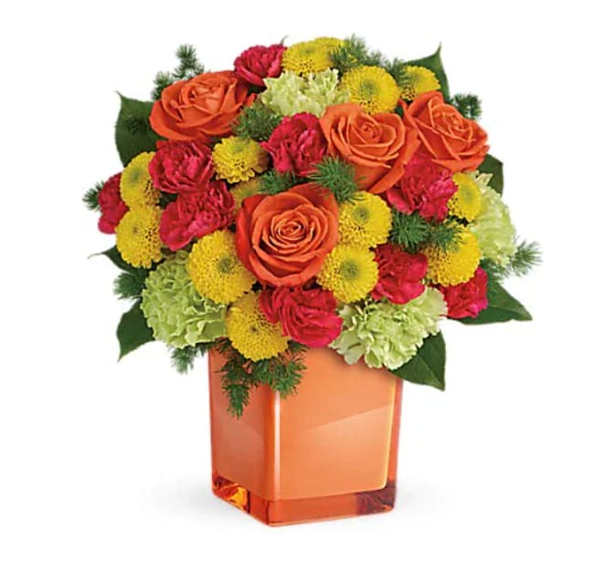 Citrus Smiles Bouquet - They brighten your days with their friendship and love, brighten theirs with these bold and beautiful blooms! Hand-delivered in a stylish glass cube, a gift in and of itself - this spirited mix of roses, carnations and mums is sure to make them smile! Bold orange roses, green carnations, dark pink miniature carnations, and yellow button spray chrysanthemums are mixed with ming fern and lemon leaf. Delivered in a glass cube. 