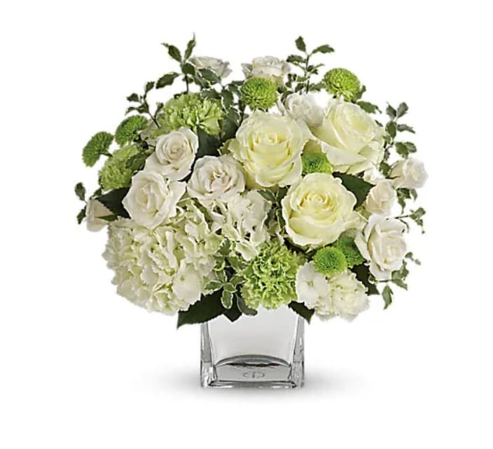 White roses and green blooms in a clear square vase