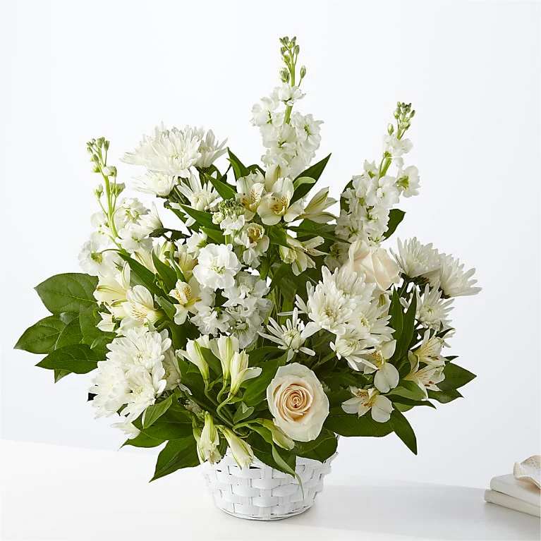 White floral arrangement in a white basket with a pale rose accent