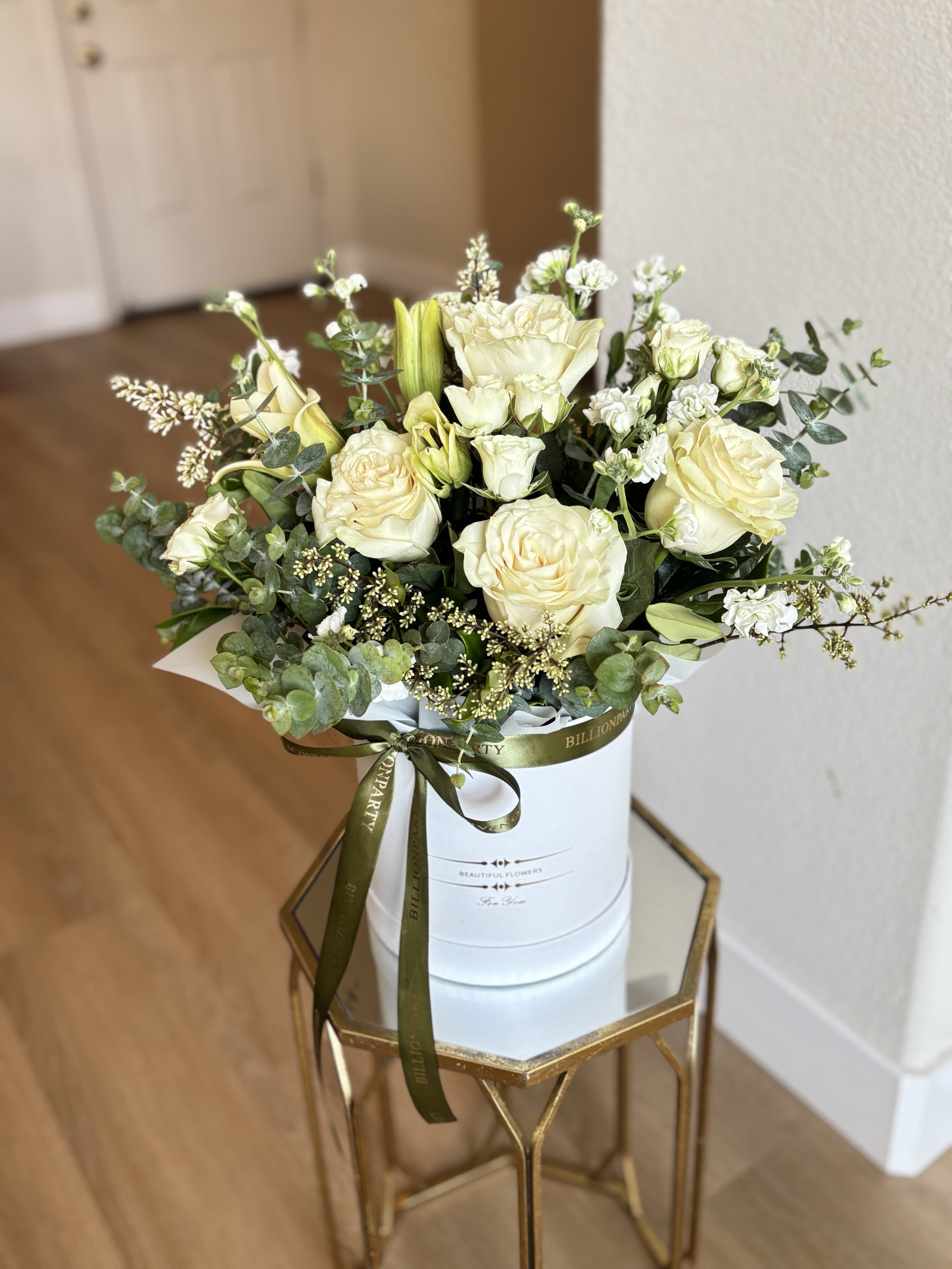 Cream roses and white blooms arranged in a white hat box with a ribbon