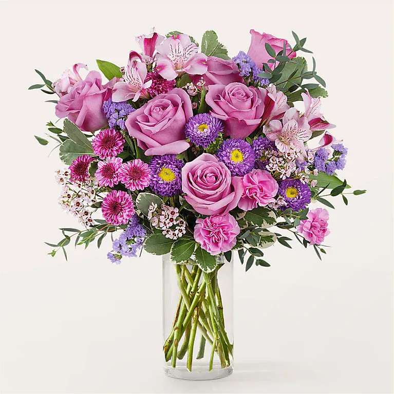 Pink roses and mixed purple flowers in a clear glass vase