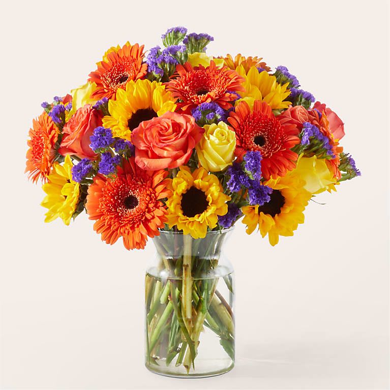 Bright mixed bouquet of gerbera daisies and roses in a clear glass vase