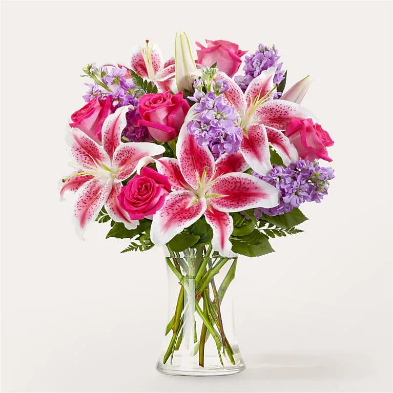 Pink roses and lilies arranged in a clear glass vase with purple flowers
