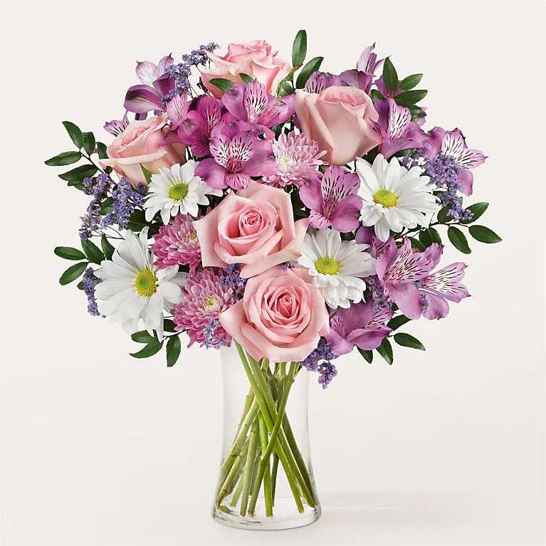 Pink roses and purple flowers arranged in a clear glass vase