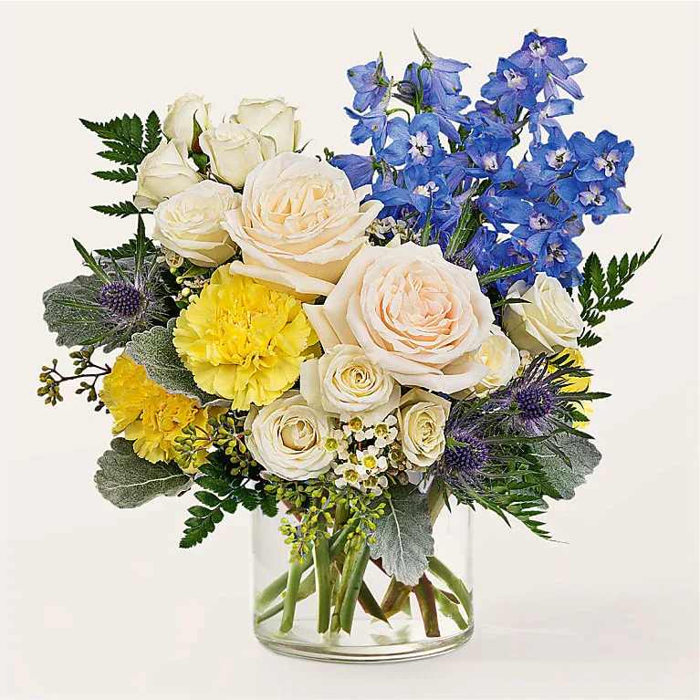 White roses and yellow carnations with blue delphinium in a clear glass vase