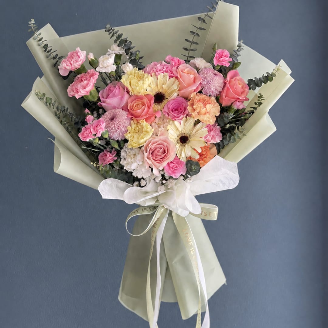 Pink and peach mixed bouquet wrapped in pale paper with a white ribbon