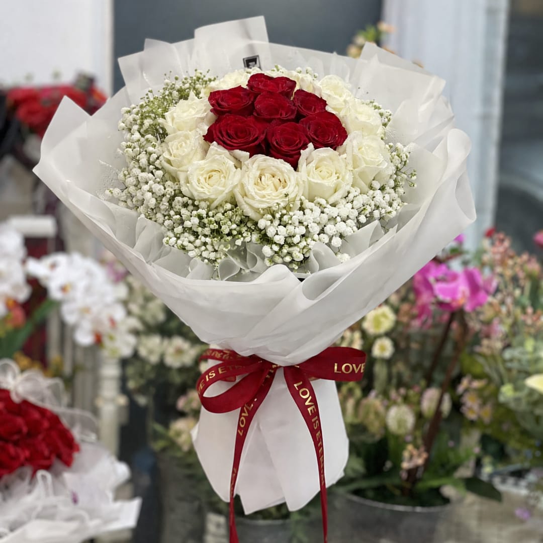 Red and white rose bouquet wrapped in white paper with a red ribbon