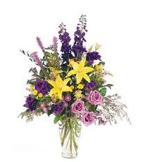 Mixed bouquet with yellow lilies, purple flowers, and pink roses in a clear vase