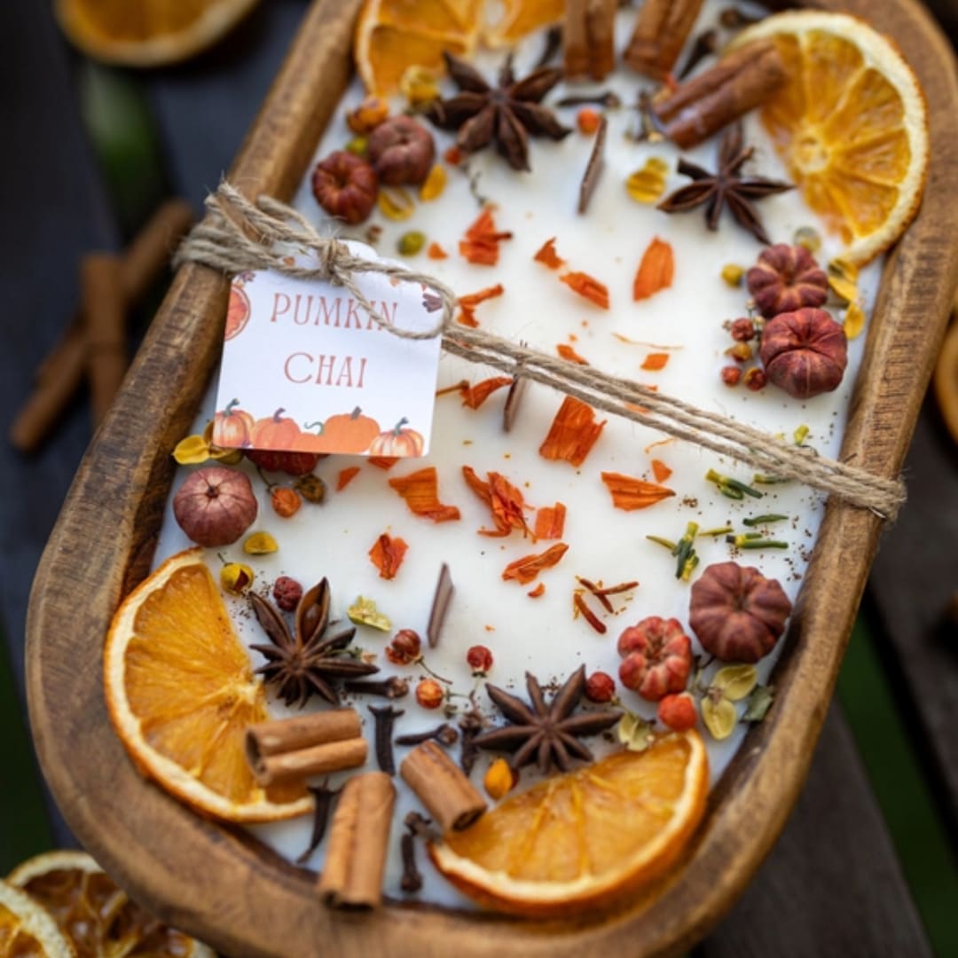Pumpkin chai candle in a wooden tray with dried orange slices and spices