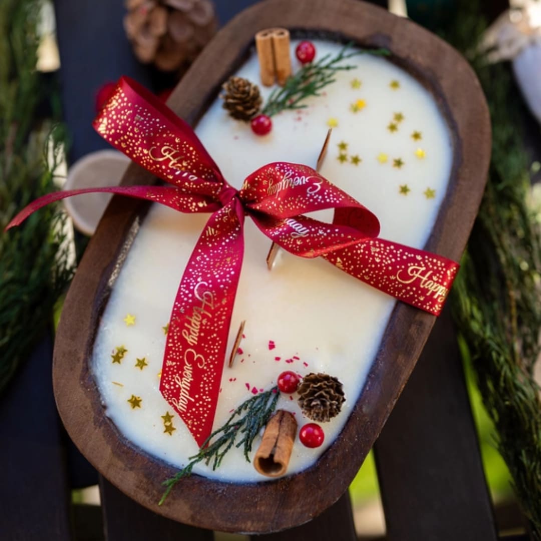 Oval holiday candle with red ribbon, pinecones, and cinnamon sticks