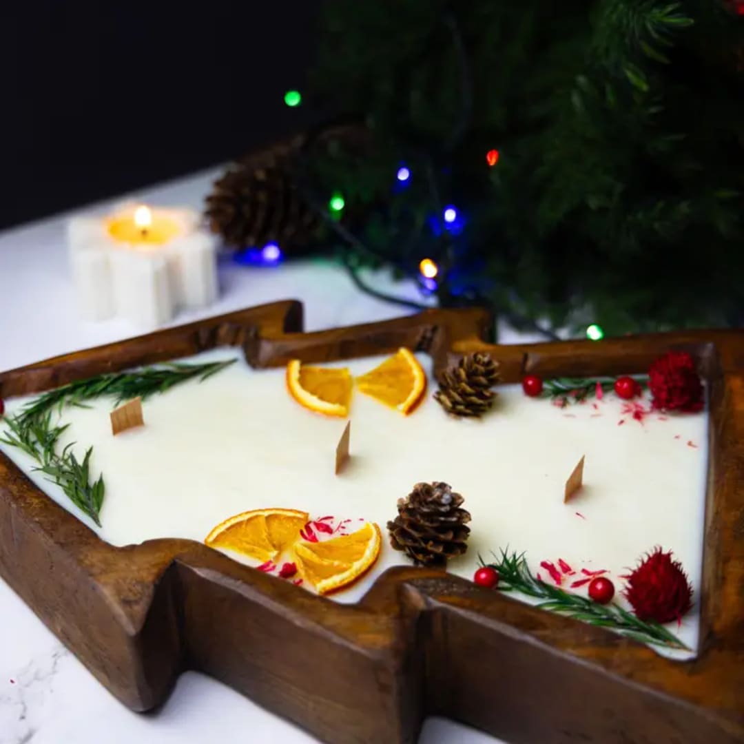 Christmas tree-shaped candle in a wooden tray with pinecones and orange slices