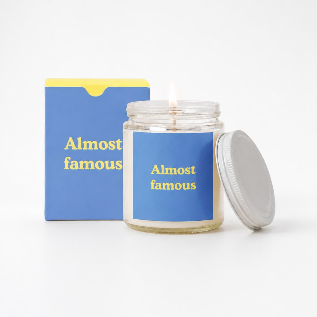 Lit candle in a glass jar with a blue label and matching box