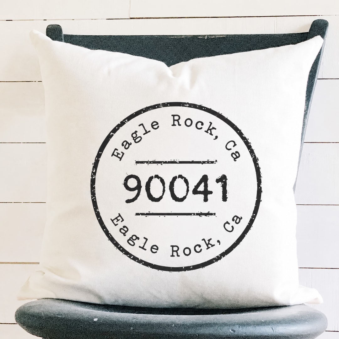 White pillow with black Eagle Rock, CA 90041 print on a dark chair