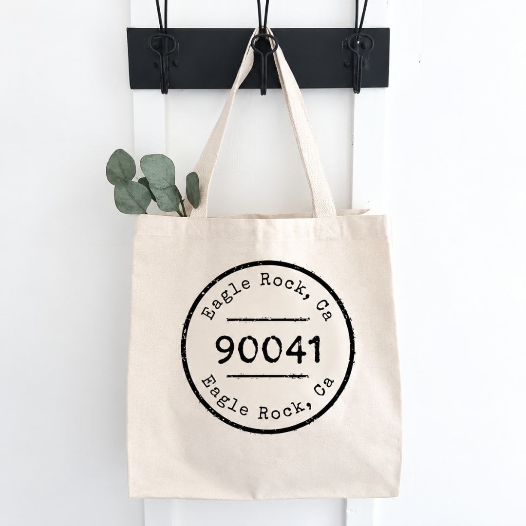 Canvas tote bag with a black printed logo hanging on a wall hook