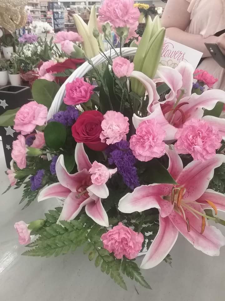 Pink lilies and carnations arranged with roses in a white basket