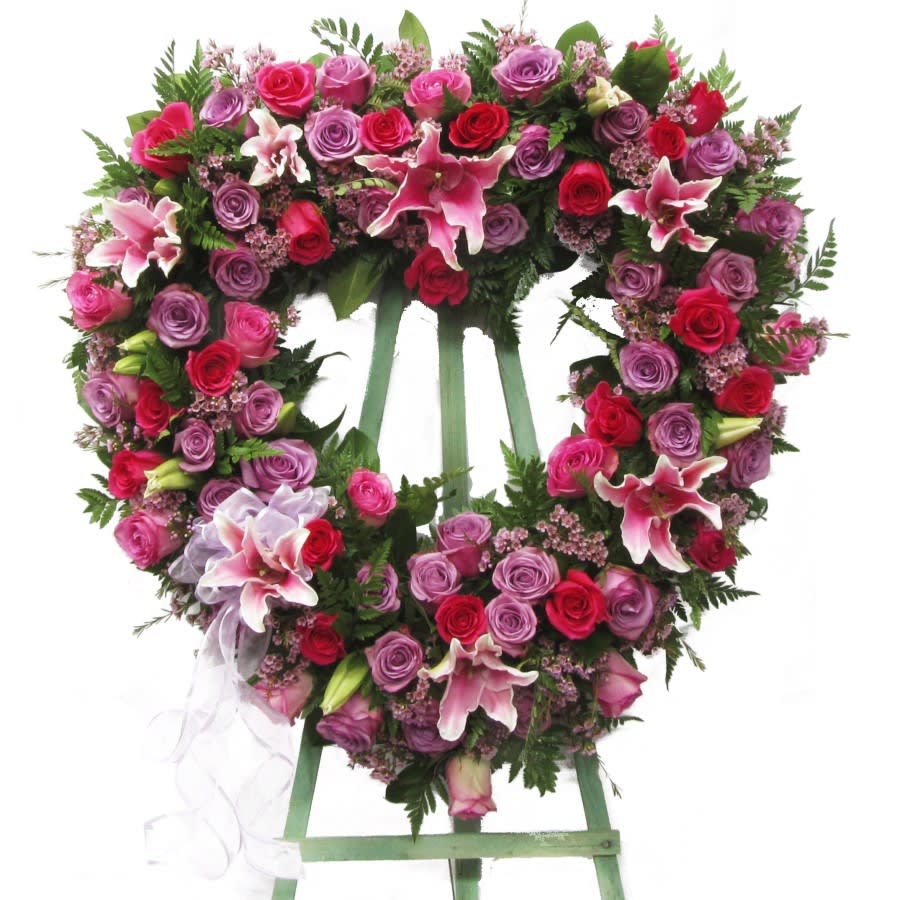 Heart-shaped floral wreath on a stand with pink and red roses and lilies