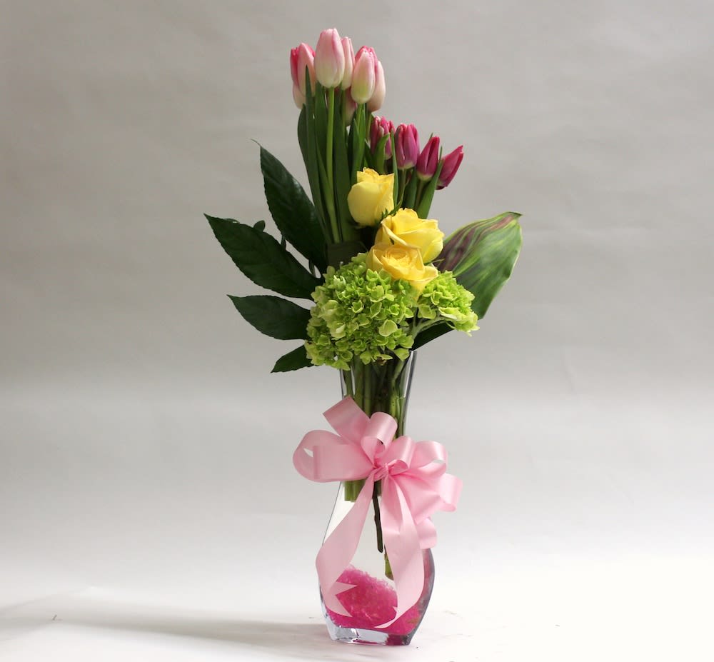 Pink and yellow tulips with green hydrangea in a glass vase with a pink ribbon
