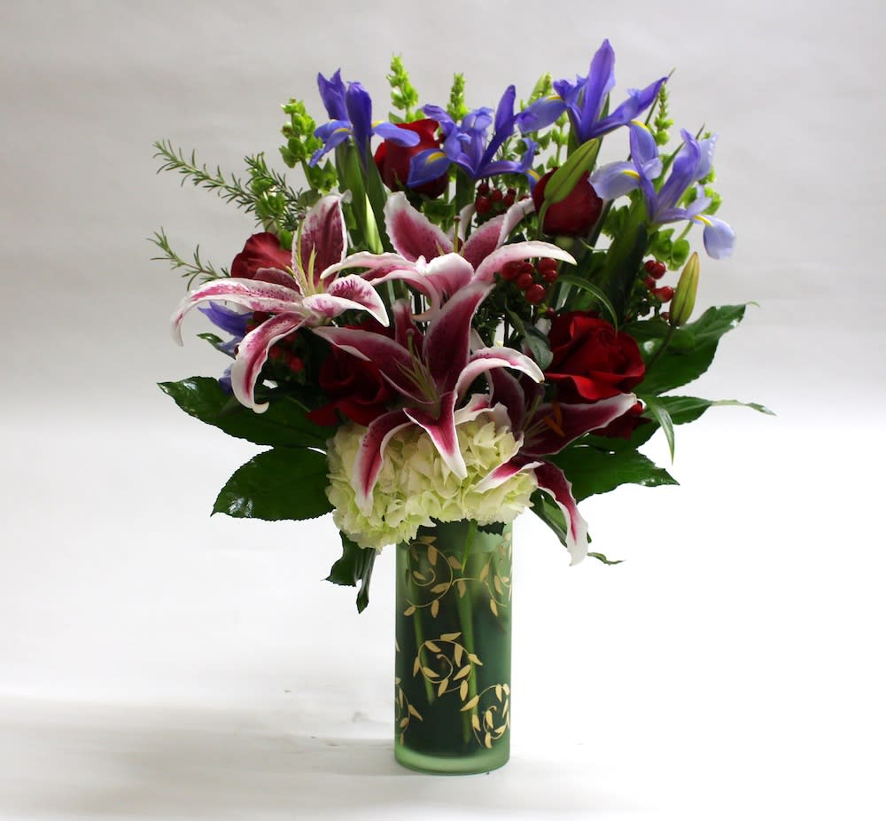 Bouquet of lilies, roses, and irises in a green glass vase