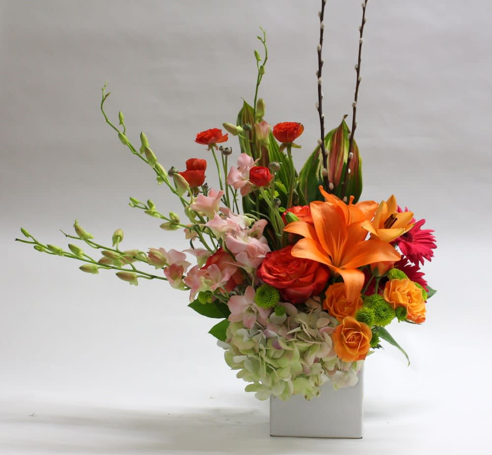 Colorful floral arrangement in a white rectangular vase with orange and pink blooms