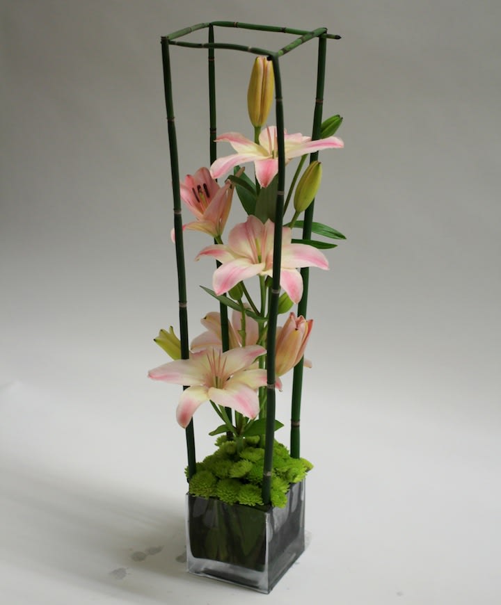 Pink lilies in a tall glass vase with bamboo supports