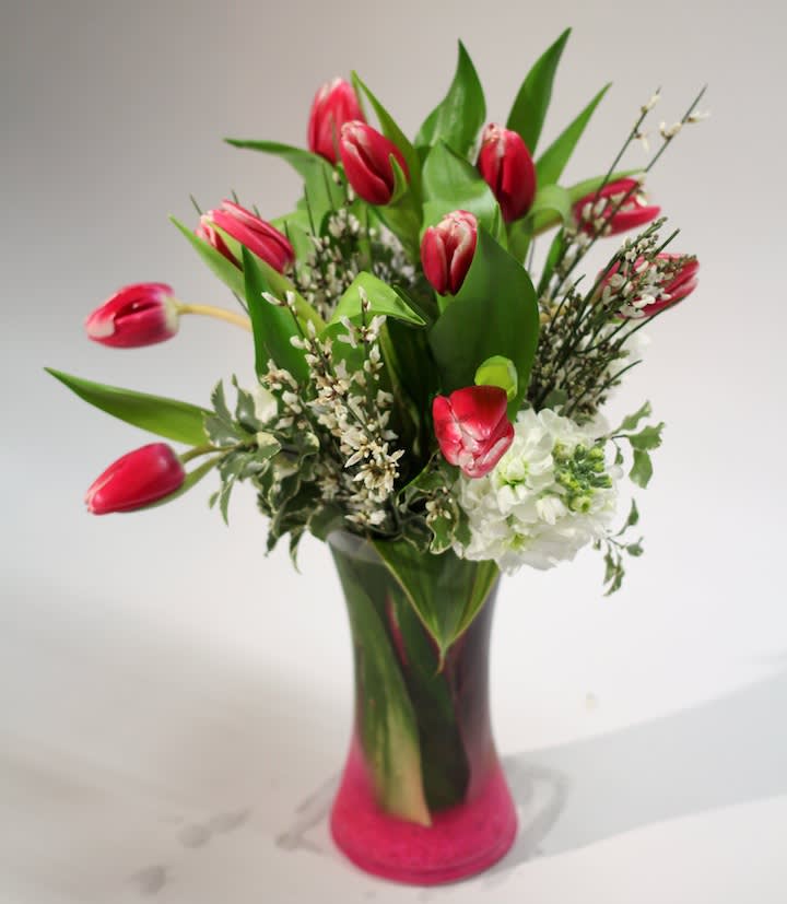 Pink tulips and white flowers in a tall glass vase