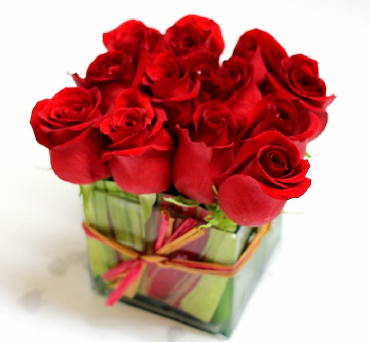 Red roses arranged in a square glass vase with a ribbon tie