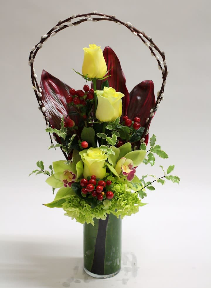 Yellow roses and green orchids in a tall vase with a decorative branch handle